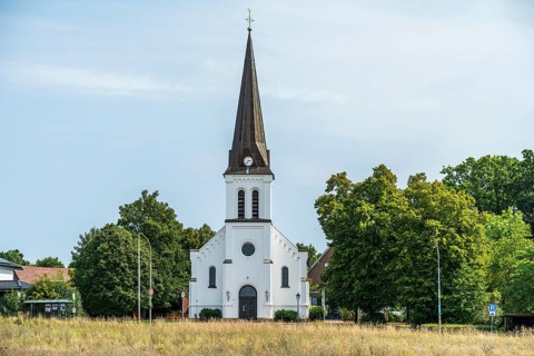 White church with tower and clock, embedded in a green landscape under a blue sky, Herford,