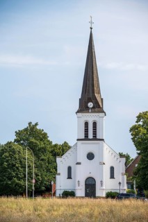 White church with high tower and clock, surrounded by trees under a clear sky, Herford, Westphalia,