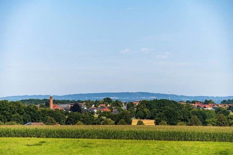 A rural view of a village surrounded by fields and trees under a blue sky, Bielefeld, Westphalia,