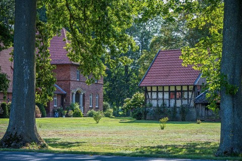 A large tiled roof house next to an older half-timbered building in a green landscape, Gütersloh,