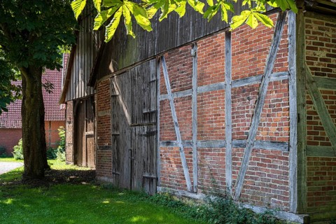 Front of a half-timbered house with wood and bricks, shaded by deciduous trees, Weser cycle path,