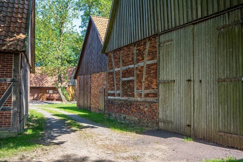 Path leads between rustic half-timbered houses made of brick and wood, surrounded by trees, Weser