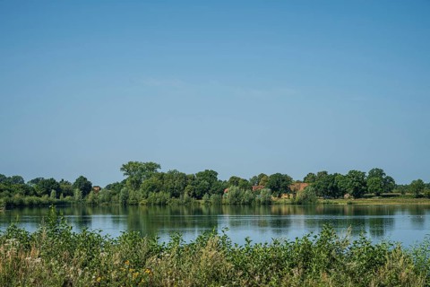 A calm river with green trees and a clear sky reflects the peaceful atmosphere of nature, Weser