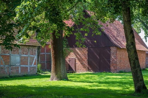Large brick and wooden barn surrounded by trees and green grass, Weser cycle path, Schlüsselburg