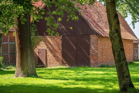 Old brick and timber barn surrounded by trees in rural area, Weser cycle path, Schlüsselburg barn