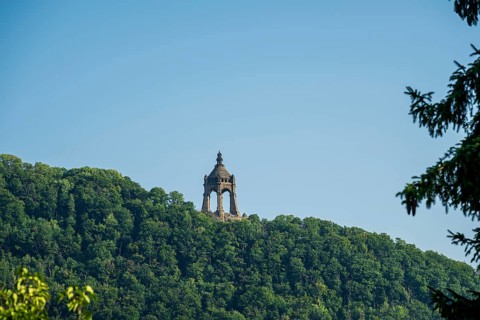 A monument rises on a wooded hill under a clear blue sky, Kaiser Wilhelm Monument,