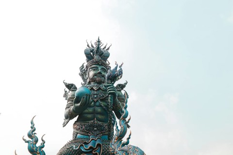 A statue of a mythical figure with intricate details against a pale sky in Wat Rong Suea Ten or