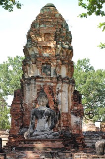 A Buddha statue seated before an ancient brick stupa, surrounded by greenery, exuding serenity in