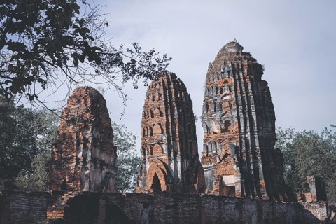 Tall brick ruins and towers reaching towards the sky amidst surrounding trees, evoking antiquity.