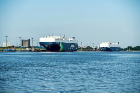 Two large cargo ships moored in the harbour, surrounded by water and blue sky, car freighters in
