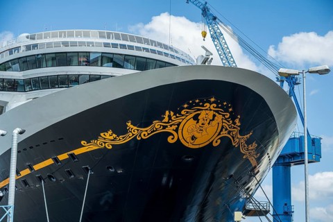 A detailed decorated bow of a cruise ship under a cloudy sky with a crane in the background, cruise