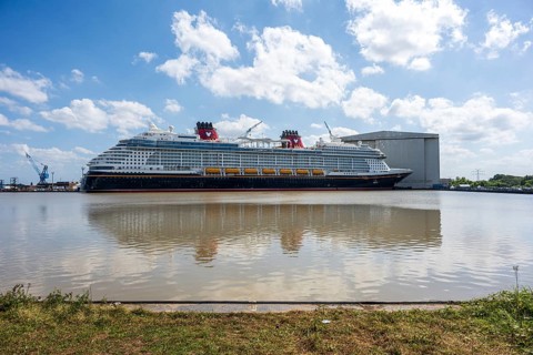 A cruise ship lies in the water, surrounded by a shipyard and a grassy embankment, cruise ship in