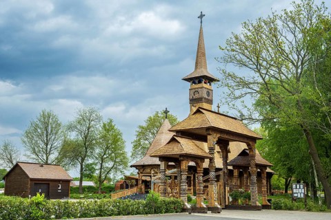 Impressive wooden church with elaborate wood carvings, surrounded by trees under a cloudy sky, The