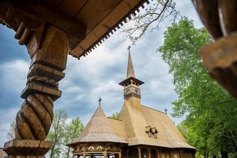 Detailed wooden church with decorative carvings and wooden roof, surrounded by trees, The Romanian