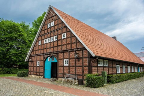 Traditional half-timbered house with red tiled roof and green surroundings under a cloudy sky,