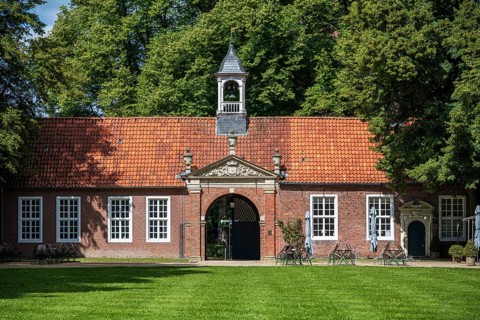 A historic building with a red tiled roof, a small bell tower, surrounded by green trees and a