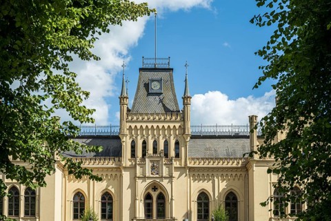 A Gothic castle with towers surrounded by green trees under a blue sky, Schloss Evenburg, Leer,