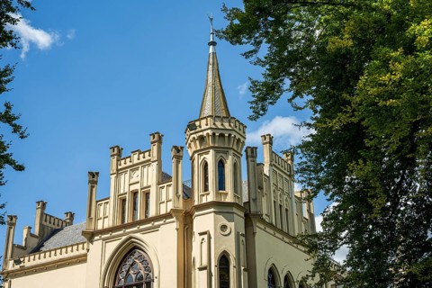 The Gothic-style castle tower rises into the blue sky, surrounded by trees, Schloss Evenburg, Leer,