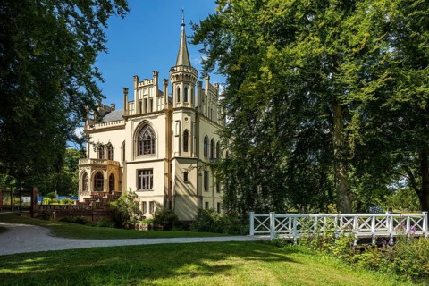 A castle in a peaceful landscape with a bridge in the foreground and a blue sky, Schloss Evenburg,