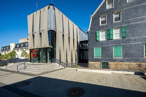 Modern glass façade next to an old house with coloured shutters, strong play of light and shadow,