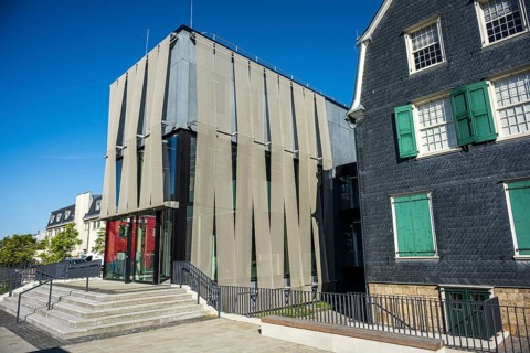 Modern building with a striking façade and large glass windows next to a traditional house under a