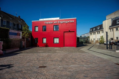 Theatre building in red with cobblestones surrounded by urban elements, high-contrast design,