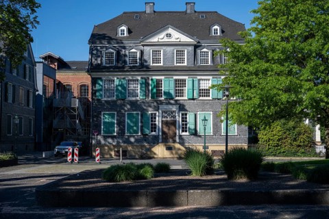 Large historic building with green shutters and surrounding trees in the sunlight, Friedrich Engels