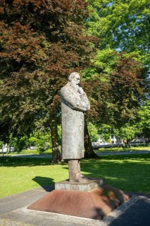 Side view of a stone statue of a pensive man in a green park with trees, statue of Friedrich Engels
