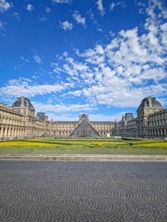 A grand panoramic view of the Louvre Palace with its iconic glass pyramid in the center under a