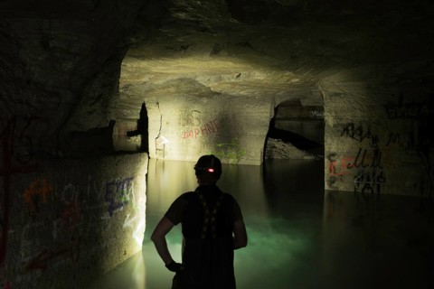 Person exploring illuminated, water-filled mine with graffiti, Ofenkaulen, Lost Place,