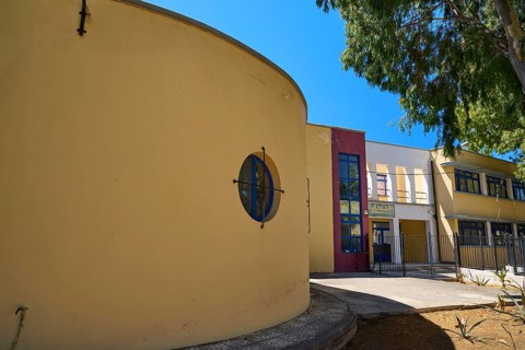 Gymnasium, Yellow modern building with round shapes, next to a tree under a blue sky, Historicism,