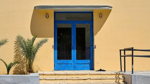 Gymnasium, A blue entrance to a yellow building with plants on the side, Historicism, Art Deco,