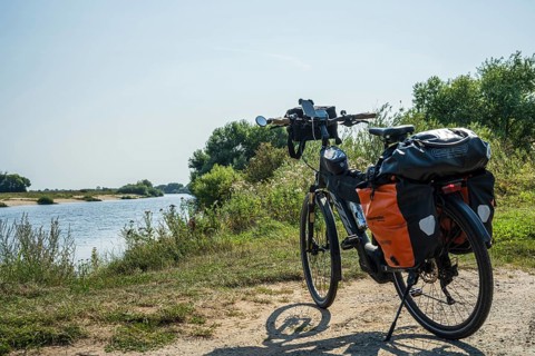 A bike with panniers stands on a sunny riverbank, embedded in nature, Weser cycle path, Weser,