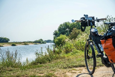 A bicycle stands on the riverbank, surrounded by a green landscape under a clear sky, Weser cycle