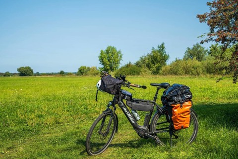 A bicycle stands on a green meadow under a blue sky, accompanied by light shadows of nature, Weser
