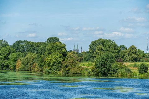A river with green foliage, church towers in the background and blue sky, Weser cycle path, Weser,