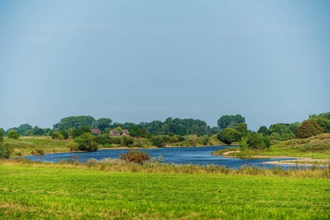 River flows through a green landscape under a blue sky, surrounded by trees and meadows, Weser