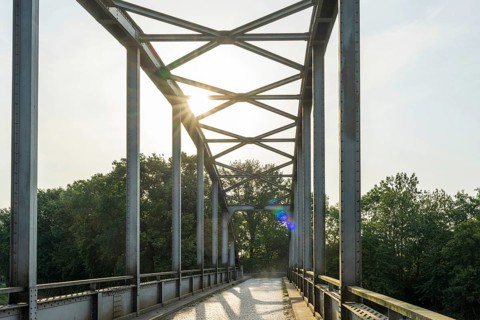 Metal bridge with sunlight, surrounded by trees, shows modern style, Weser cycle path, district of