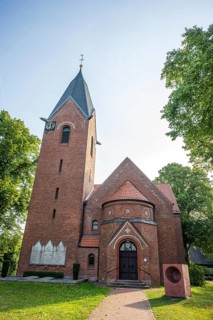 Brick church with Gothic tower and clock, surrounded by green trees under a blue sky, Weser cycle