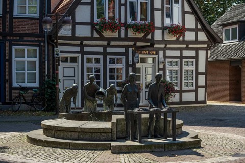 Sculptures at a fountain in front of a traditional half-timbered house in a quiet city street,