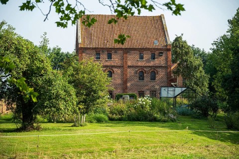 A large brick building with garden, surrounded by trees and vegetation on a summer's day, Bücken,