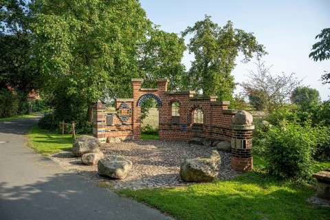 Brick wall with archway in a sunny park next to a path and trees, Bücken, district of Nienburg