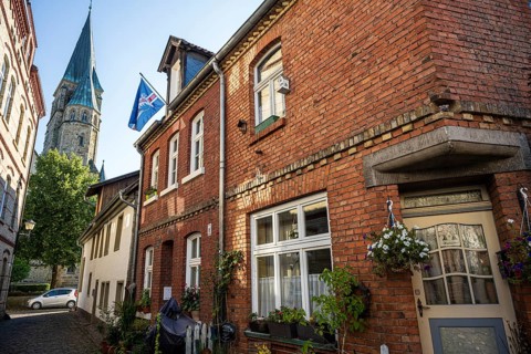 Brick houses with church in the background, surroundings full of plants and flags, Warendorf,