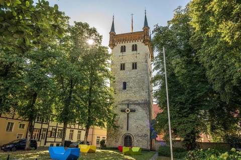Tower in the town park with colourful chairs and flag, surrounded by tall trees, tower of the old