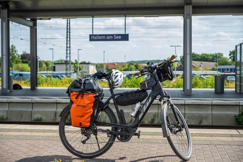 A bicycle with panniers stands at Haltern am See station, surrounded by summery nature and railway