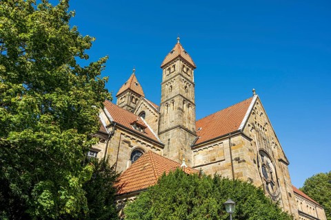 Gothic church with red tiled roofs, surrounded by green trees under a blue sky, St. Mary's Church
