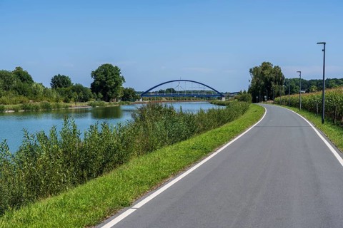 Cycle path along a river with a view of a bridge and green landscape, Dortmund-Ems Canal near