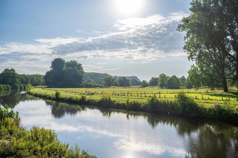 Sunny day by a river, green meadow and trees in the distance under a bright sky, Ems near