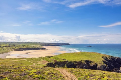 Sunny seascape view in a coastal landscape with a sandy beach and a rocky coastline from a meadow,