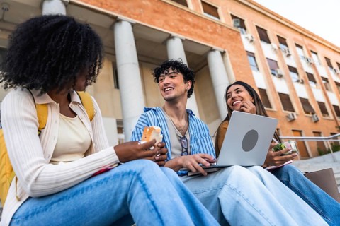 Group of happy young multiracial students sitting on steps outside a university building, enjoying